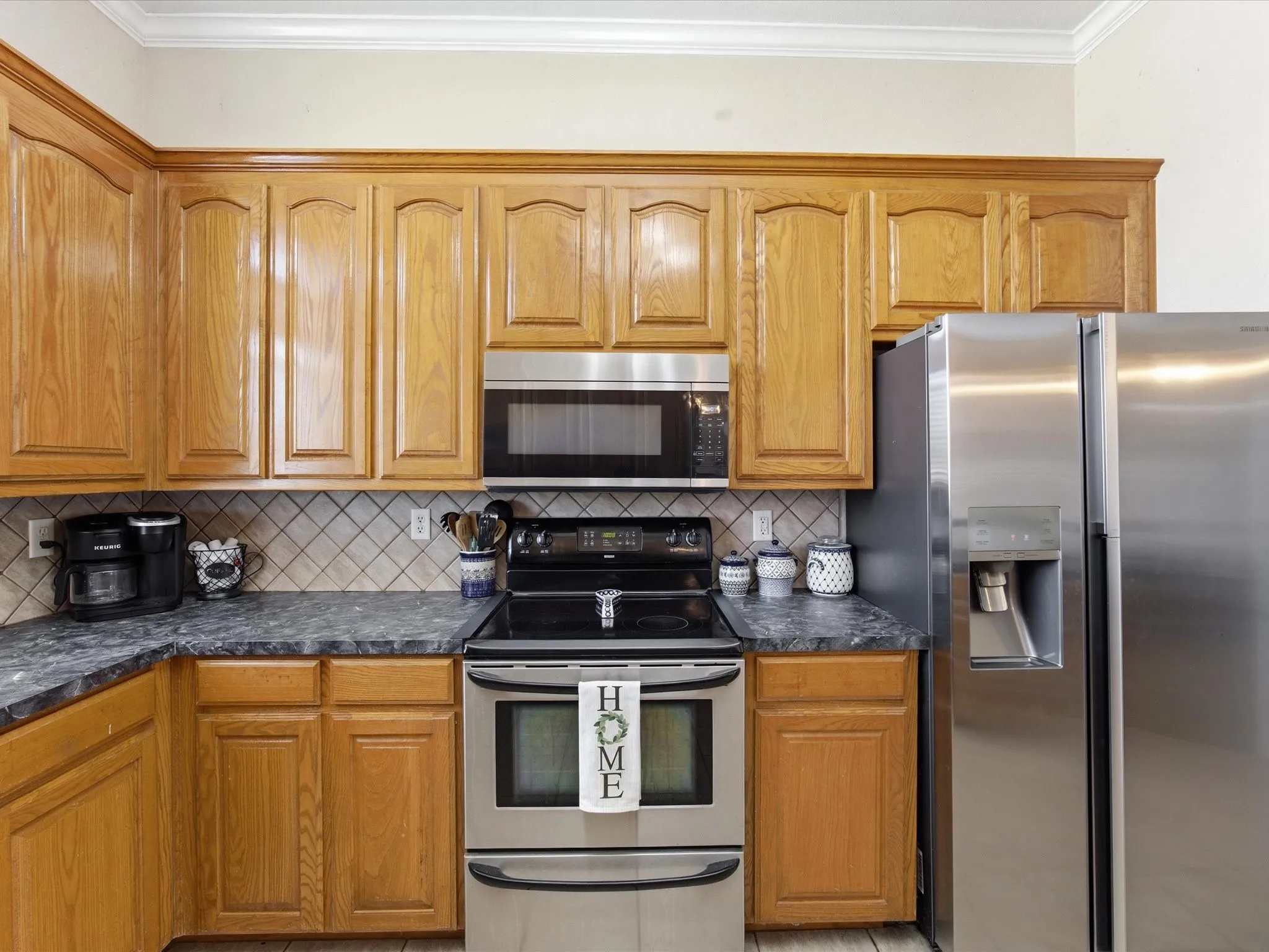 Kitchen featuring stainless steel appliances, wood finish cabinetry, crown molding, and decorative backsplash