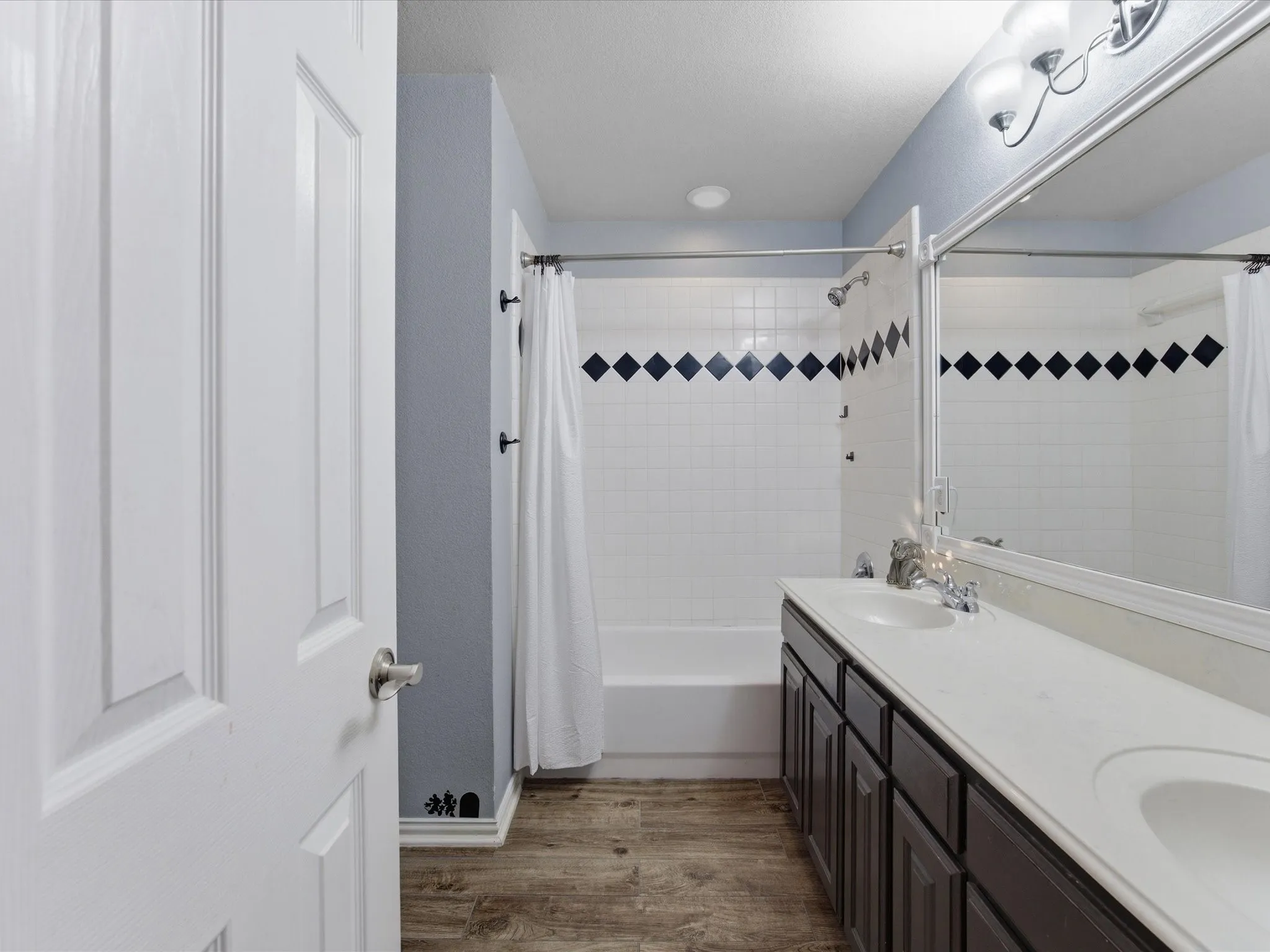 Full bath with double vanity, dark wood-style flooring, and shower / tub combo