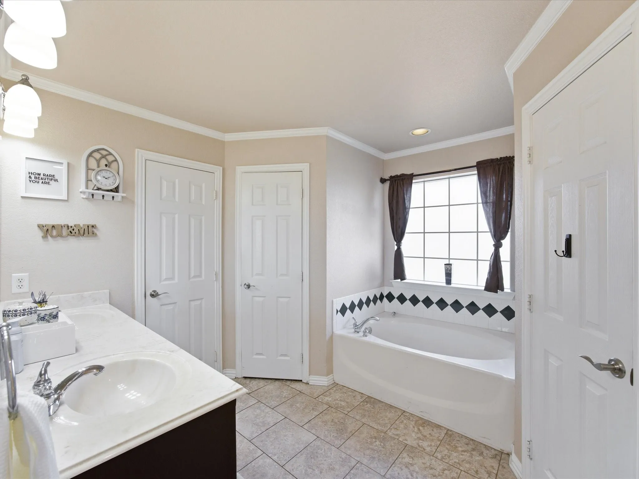 Master bath with double vanity, a bath, ornamental molding, and light tile patterned floors