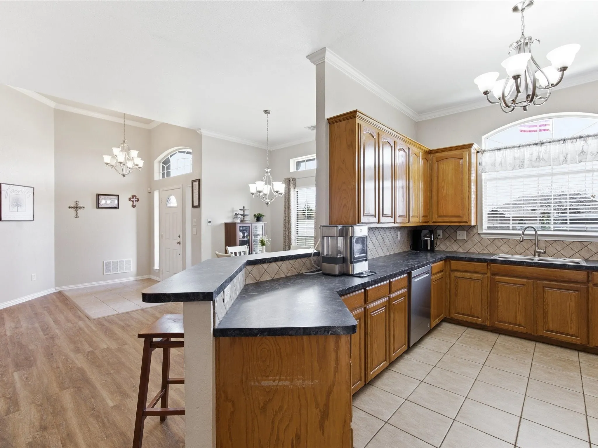 Kitchen featuring suspended lighting, wood finish cabinetry, dark countertops, a peninsula, and a kitchen breakfast bar