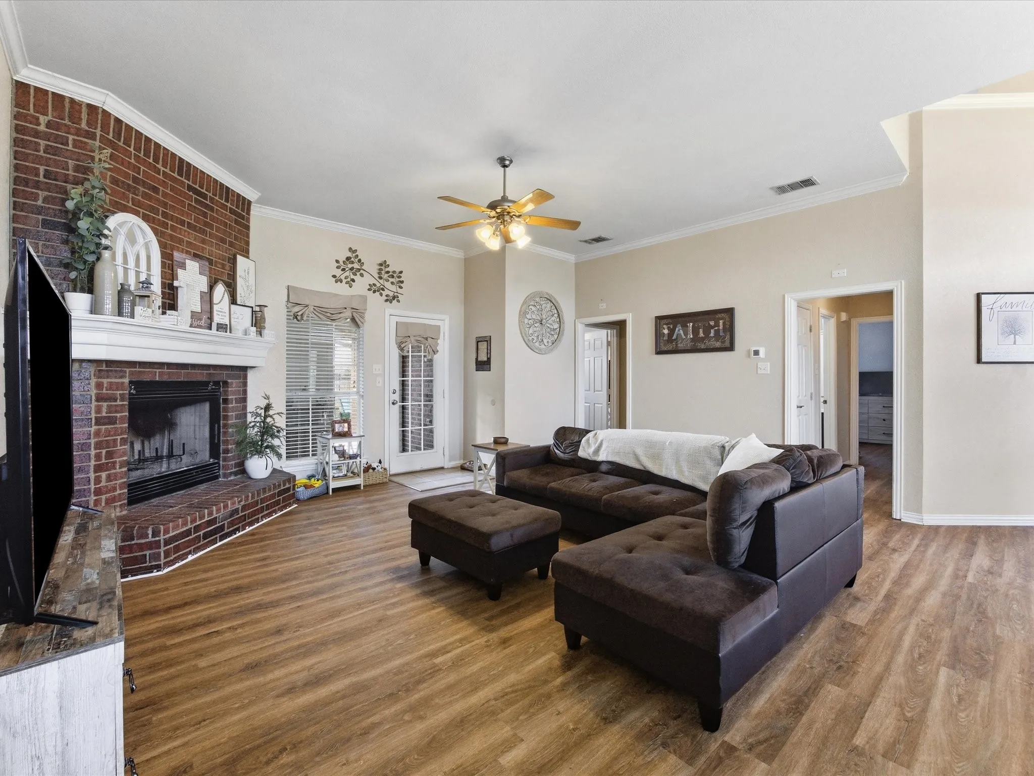 Living area with wood finished floors, ceiling fan, a brick fireplace, and crown molding