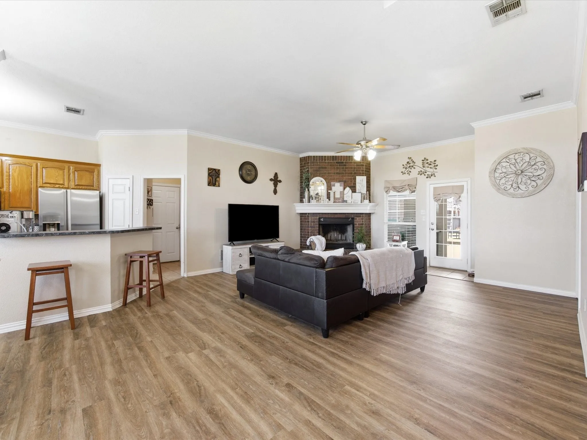 Living area featuring a ceiling fan, light wood finished floors, a brick fireplace, and ornamental molding