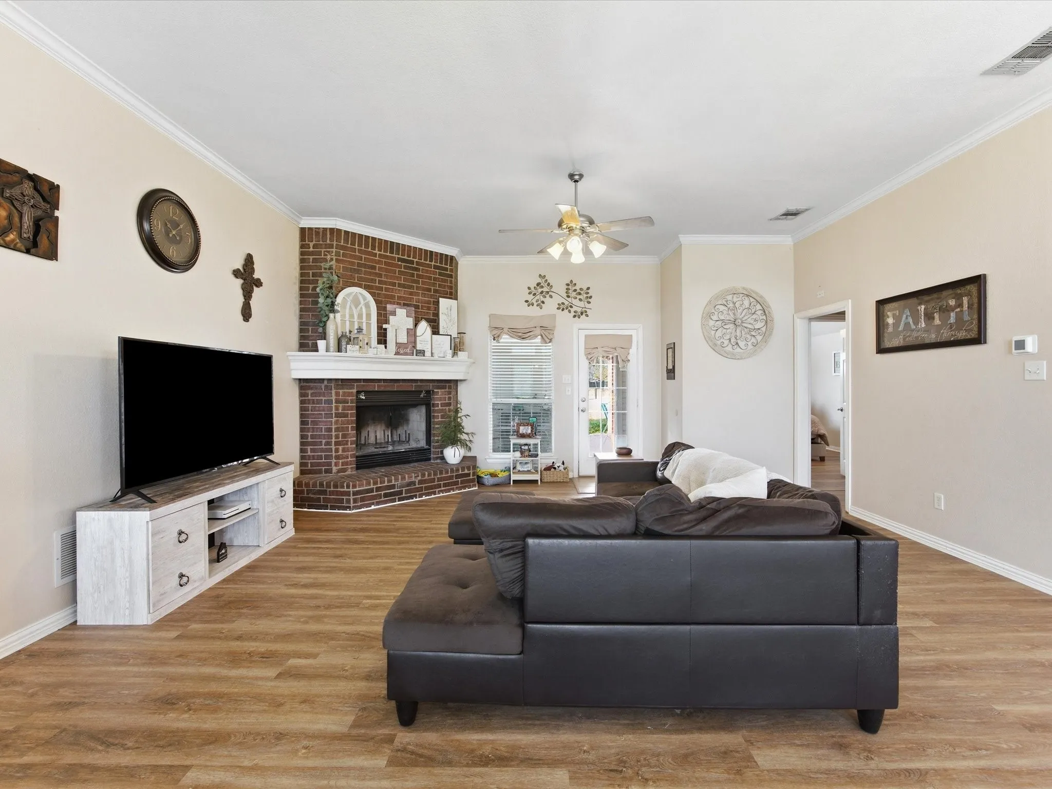 Living area featuring a ceiling fan, light wood finished floors, crown molding, and a brick fireplace