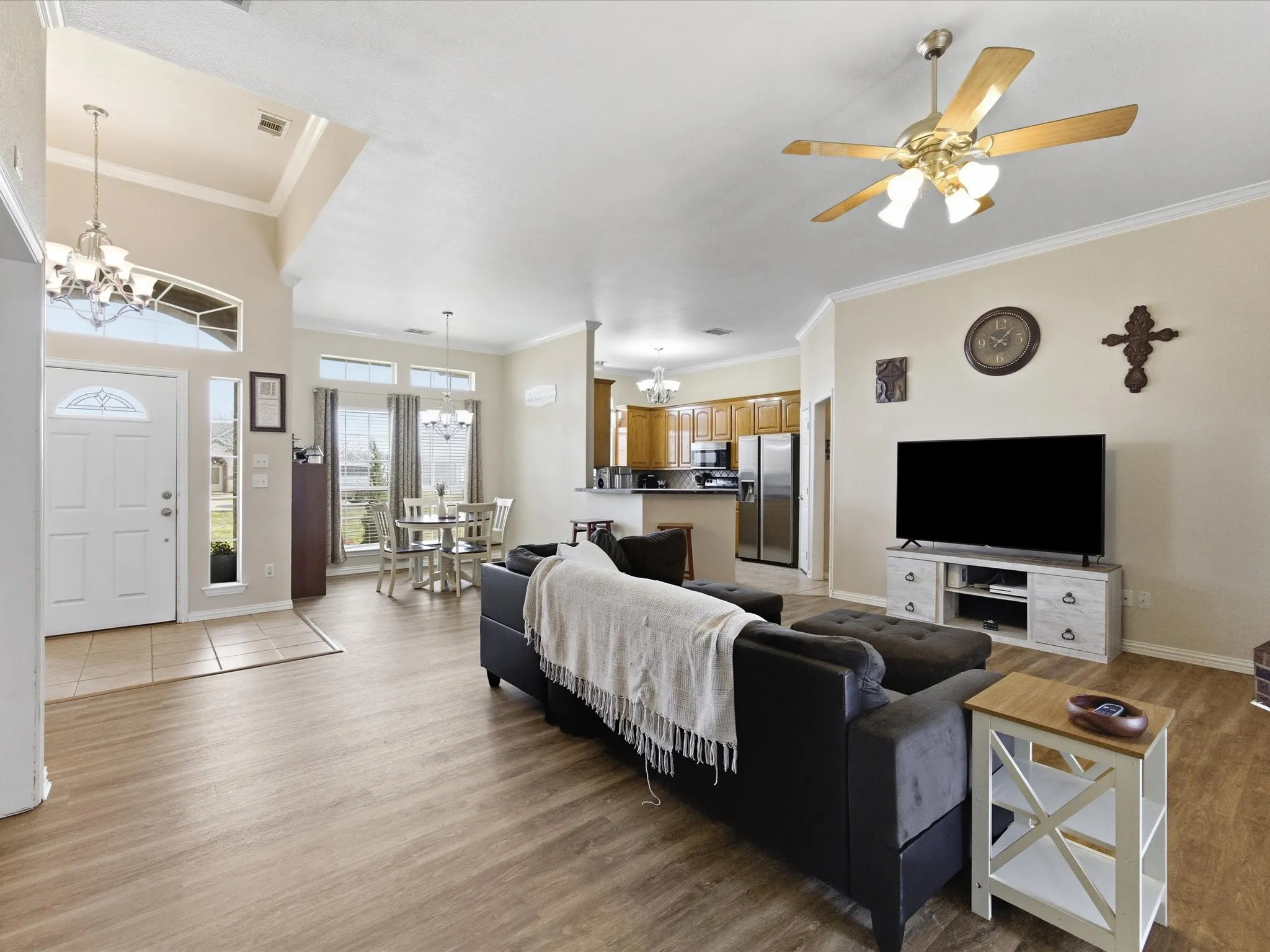 Living area with suspended lighting, ornamental molding, light wood-style flooring, and a ceiling fan