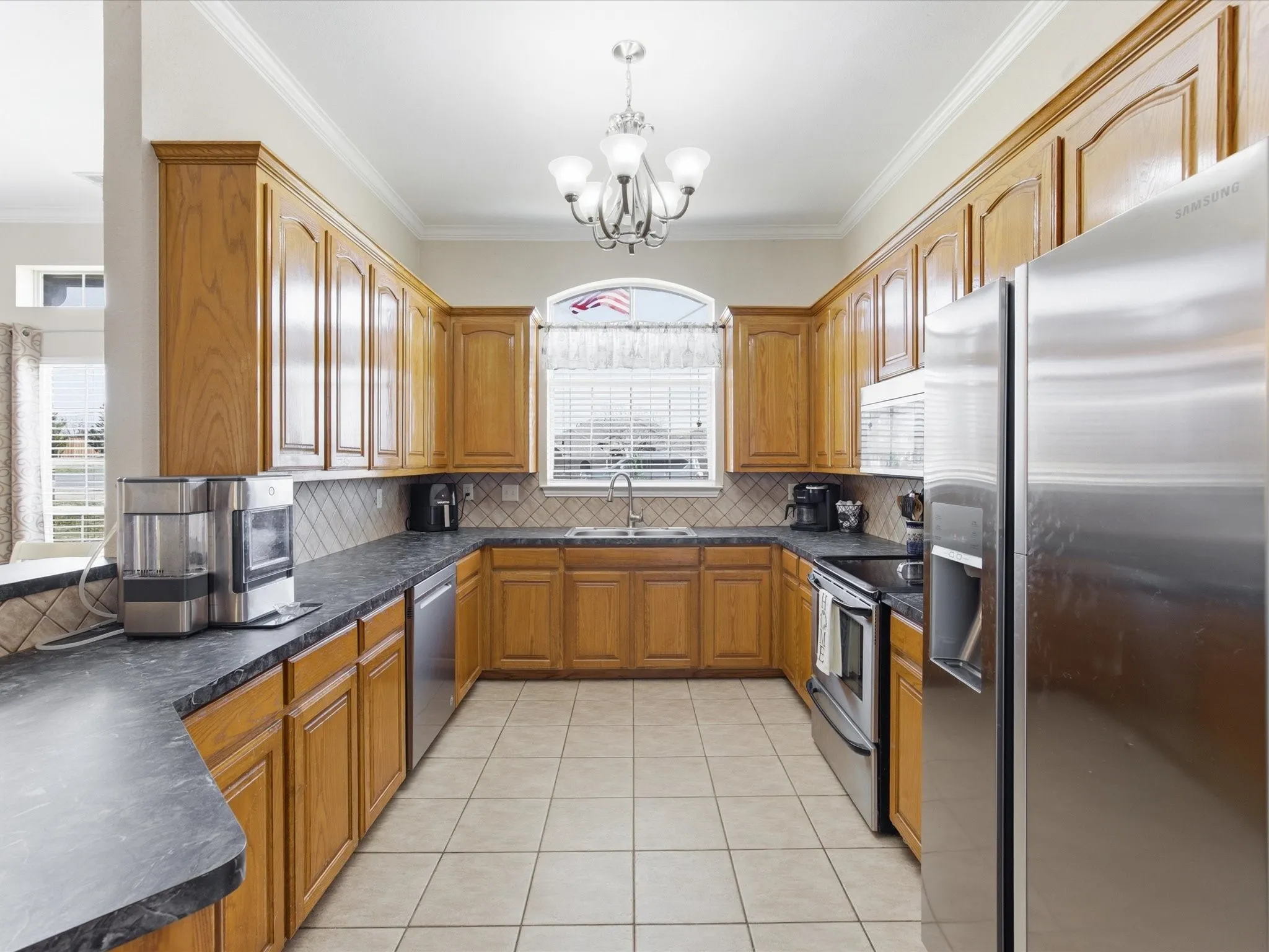 Kitchen featuring stainless steel appliances, dark countertops, wood finish cabinetry, crown molding, and a chandelier