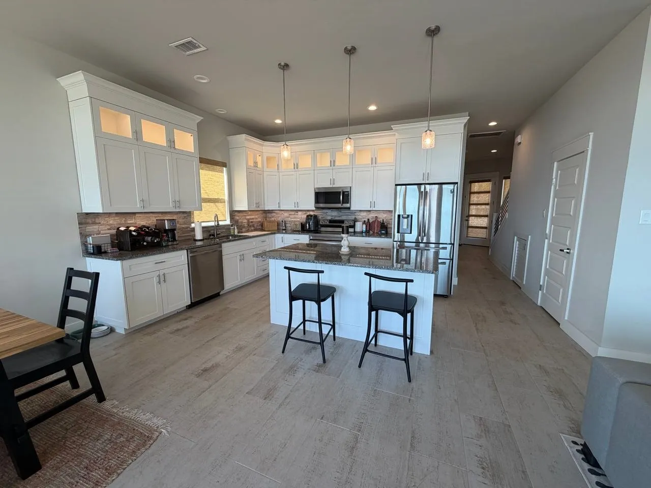 Kitchen with stainless steel appliances, white cabinets, dark stone countertops, and glass fronted cabinets