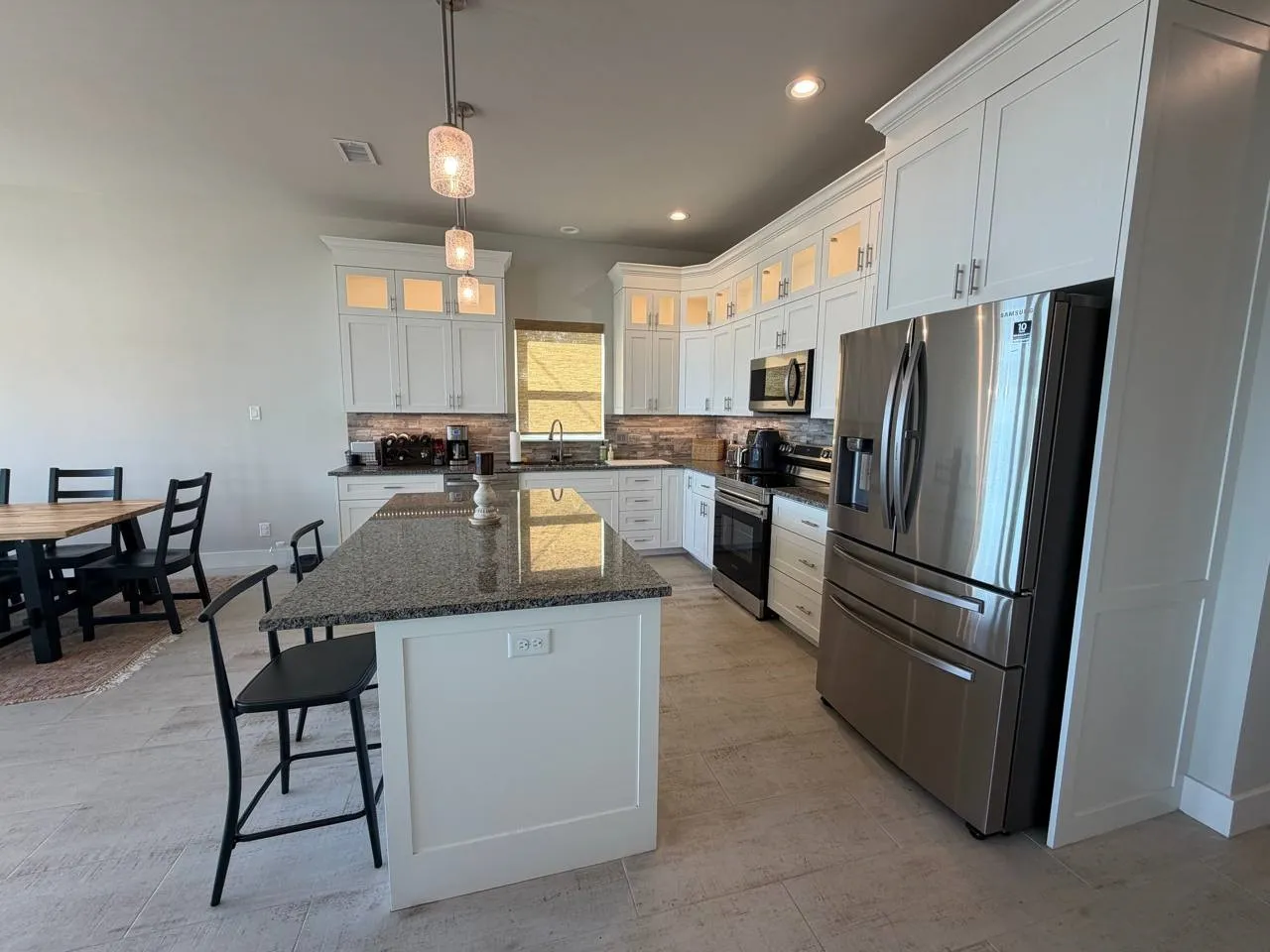 Kitchen with glass insert cabinets, a kitchen bar, dark stone counters, stainless steel appliances, and white cabinets