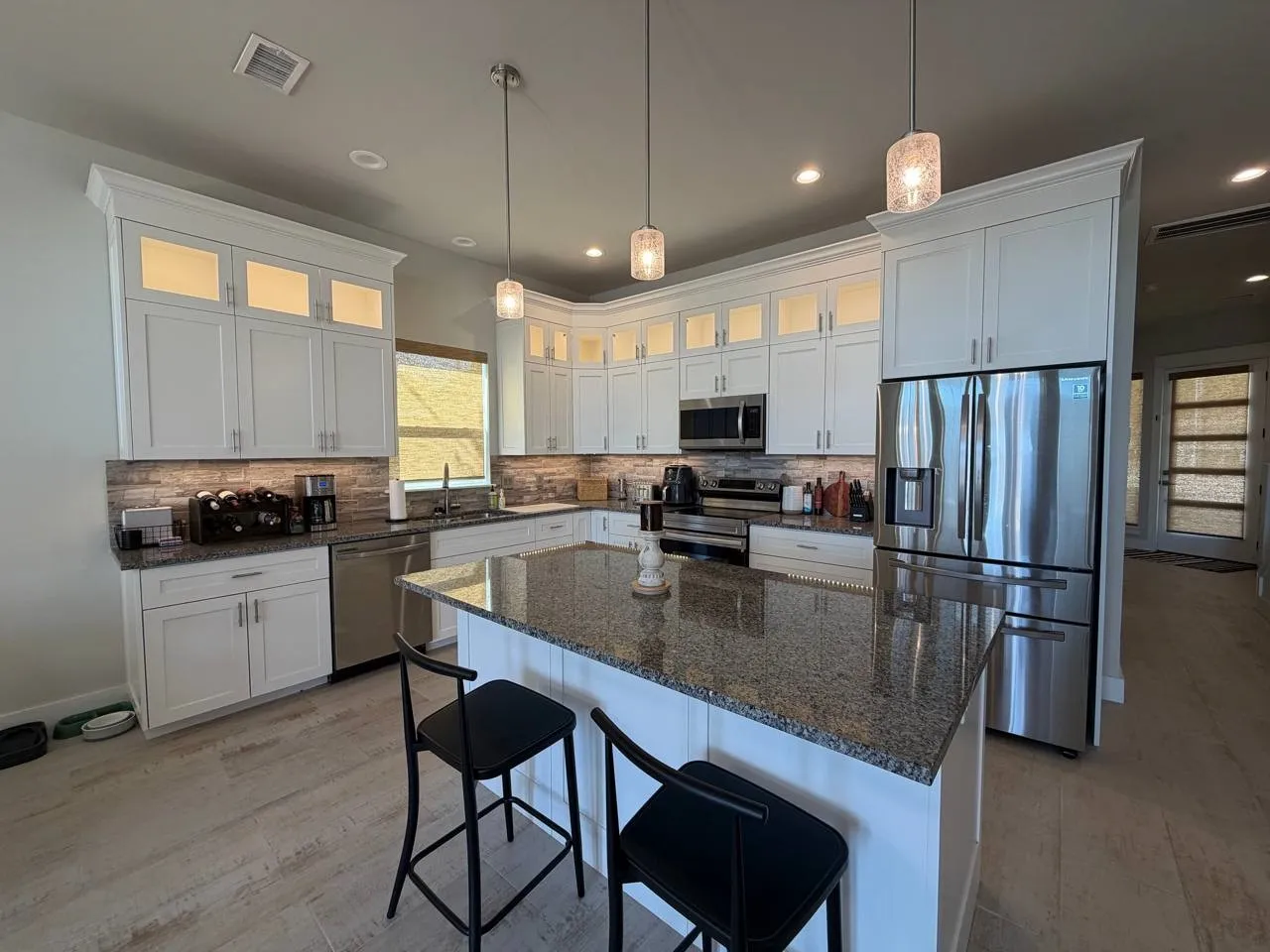 Kitchen with glass fronted cabinets, a breakfast bar area, light wood finished floors, stainless steel appliances, and dark stone counters