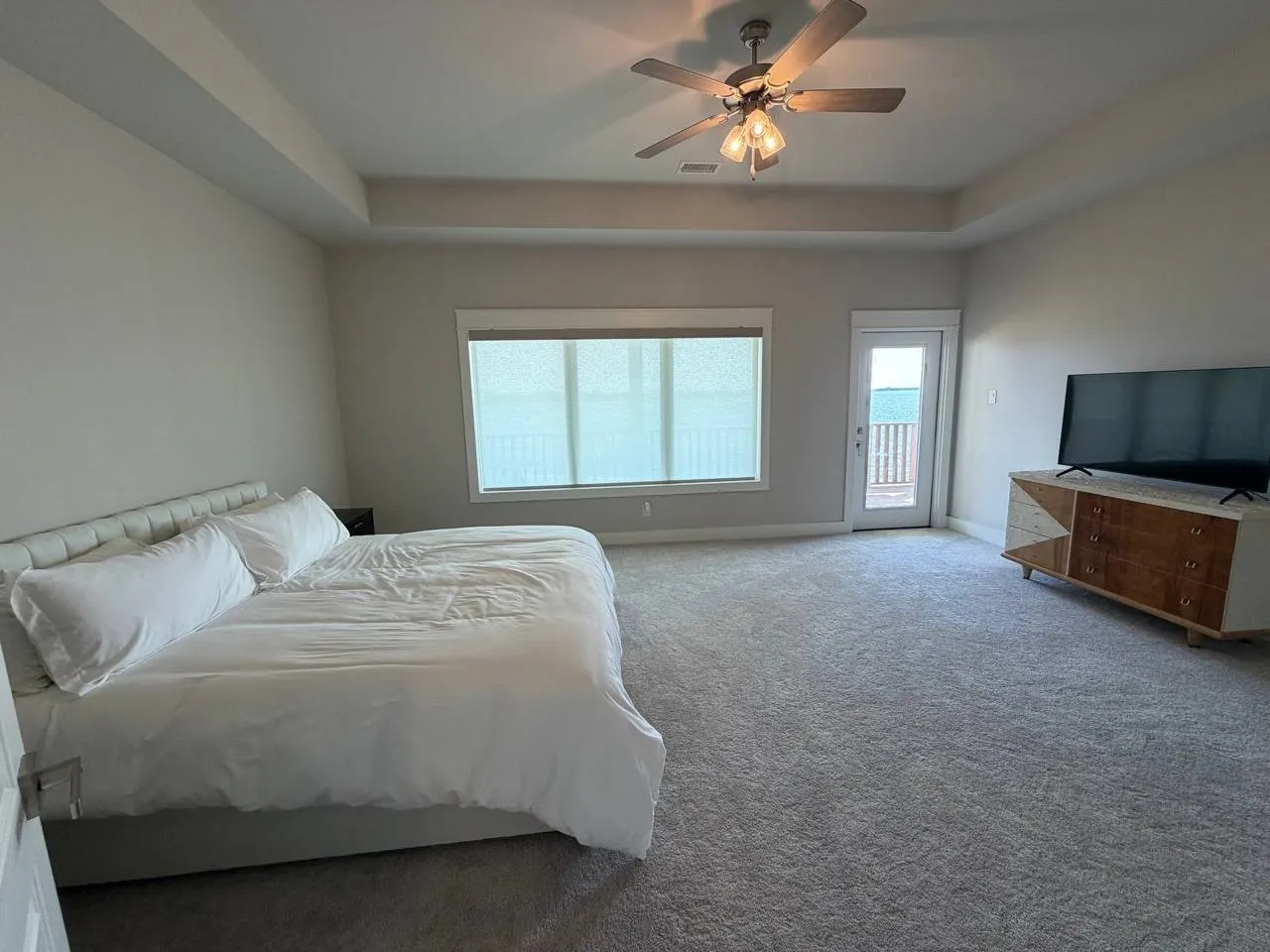 Carpeted bedroom featuring a tray ceiling, access to exterior, and ceiling fan