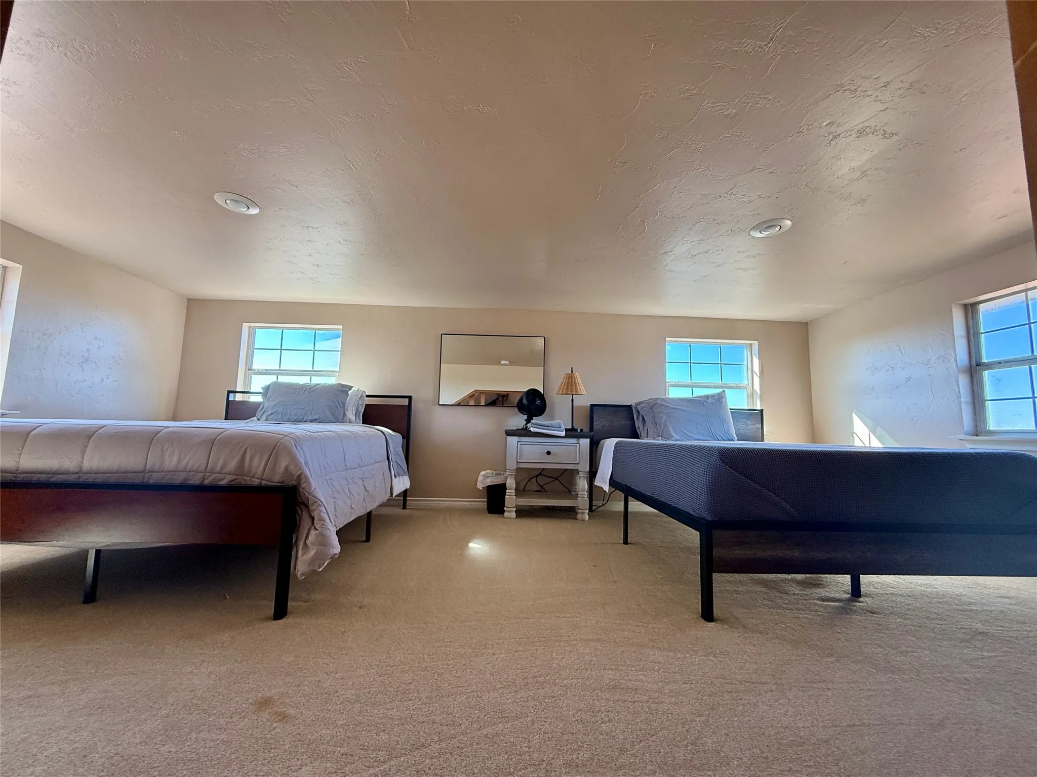 Bedroom with light colored carpet, a textured ceiling, and multiple windows