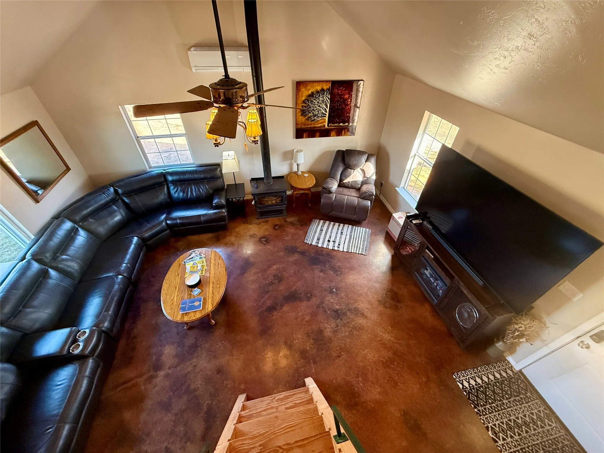 Living area with a wood stove, ceiling fan, finished concrete floors, and vaulted ceiling