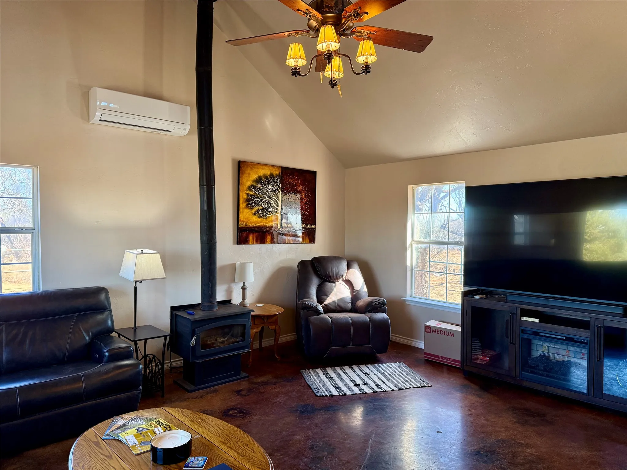 Living area featuring finished concrete floors, a wood stove, ceiling fan, and lofted ceiling