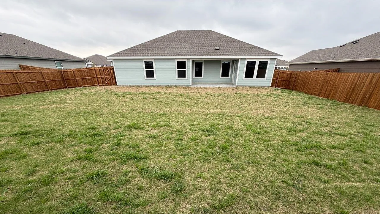 Expansive grassed backyard featuring a wooden privacy fence, a concrete patio, and light blue siding
