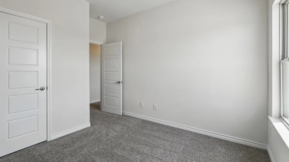 Neutral-toned room featuring a window with white trim, gray plush carpeting, and white baseboards