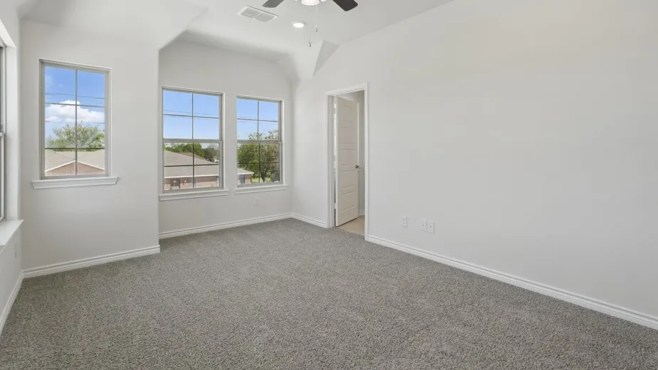 Spacious room featuring vaulted ceilings, gray carpet flooring, multiple paneled windows, and a ceiling fan with integrated lighting
