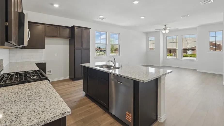Open-concept kitchen and living area featuring wood-finish flooring, dark wood cabinetry, and light-colored countertops