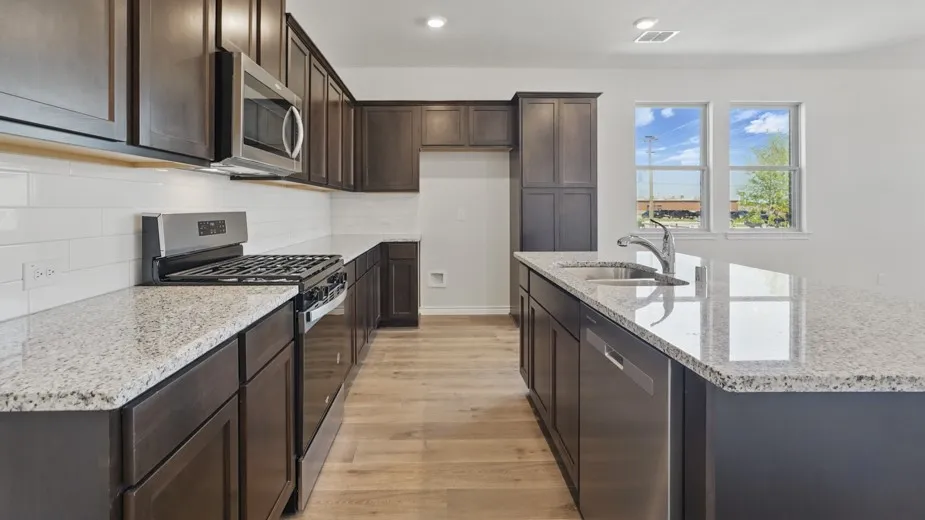 Kitchen featuring dark wood cabinetry, light granite-style countertops, and stainless steel appliances including a gas range, microwave, and dishwasher