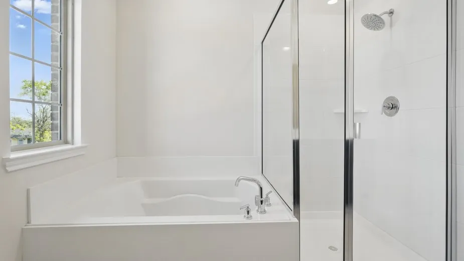 Sleek bathroom featuring a built-in soaking tub with chrome fixtures, a glass-enclosed shower with a rainfall showerhead, and a multi-pane window