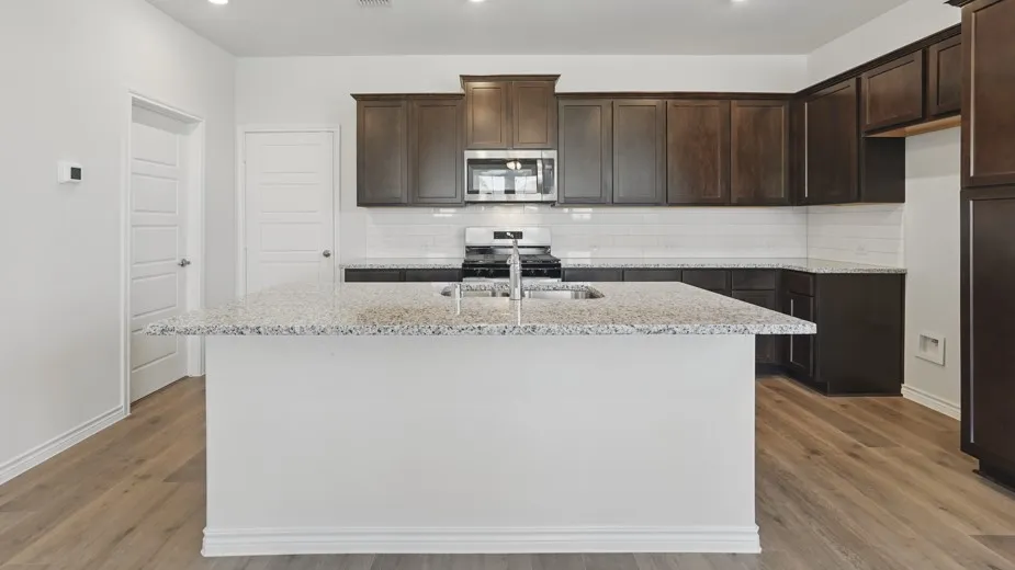 Kitchen featuring a central island with a speckled countertop, dark wood-finish cabinetry, stainless steel appliances, a subway tile backsplash, and light wood-finish flooring
