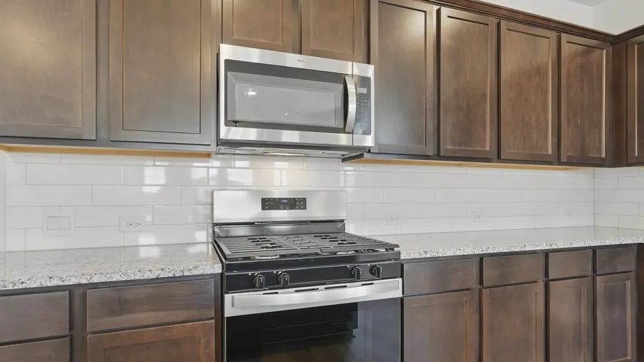 Kitchen featuring dark wood-finish cabinetry, light speckled countertops, a subway tile backsplash, stainless steel range, and an over-the-range microwave