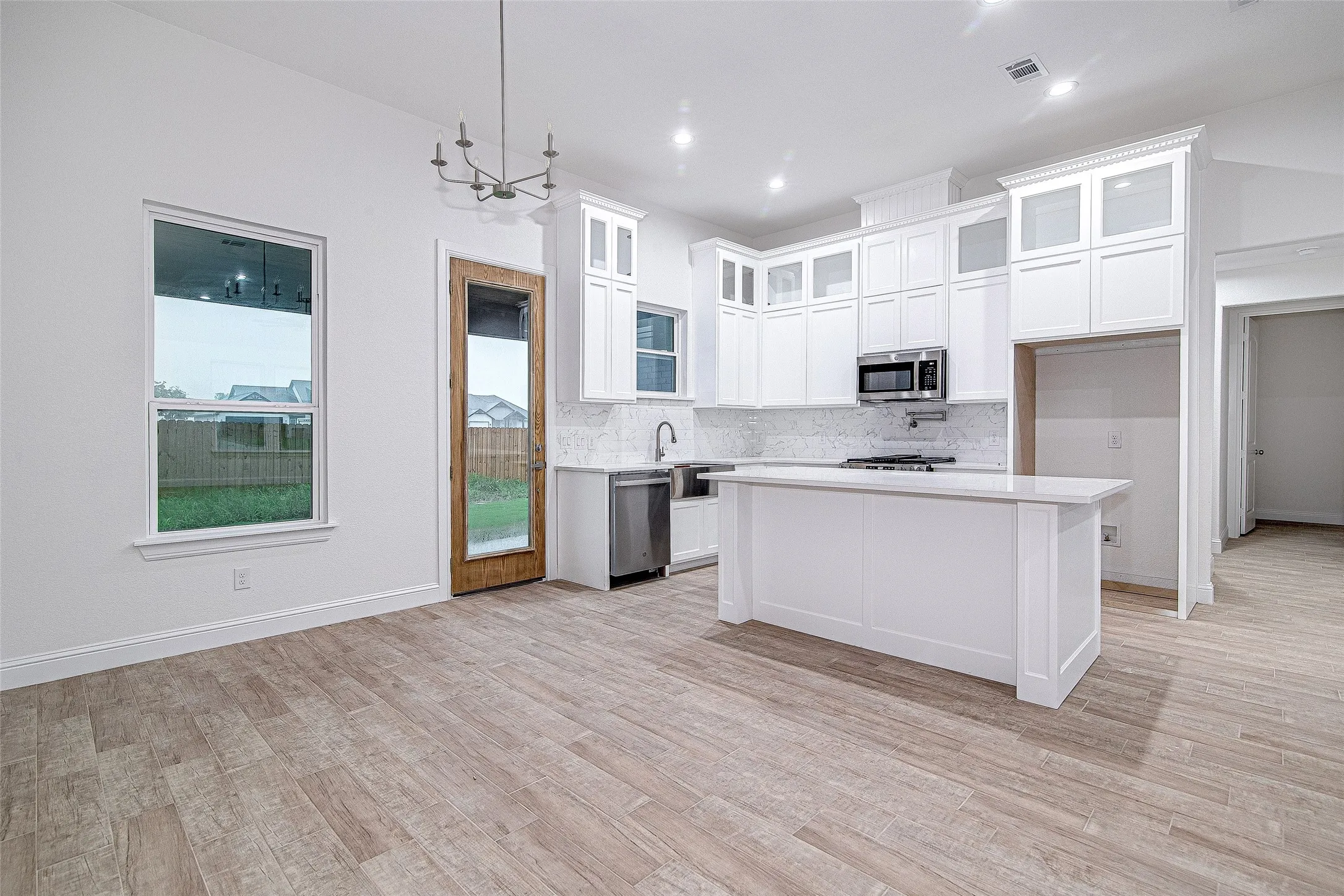 Kitchen with stainless steel appliances, light countertops, backsplash, light wood-style floors, and white cabinets