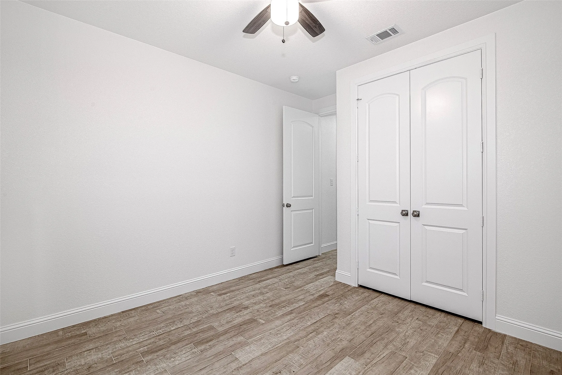 Unfurnished bedroom with light wood finished floors, a closet, baseboards, and a ceiling fan