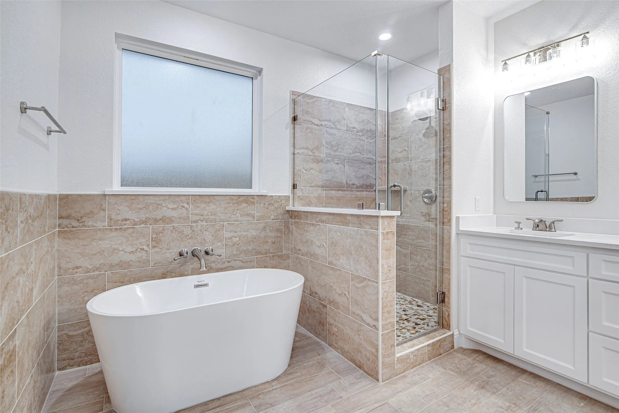 Full bathroom featuring tile walls, a shower stall, a freestanding bath, vanity, and a wainscoted wall