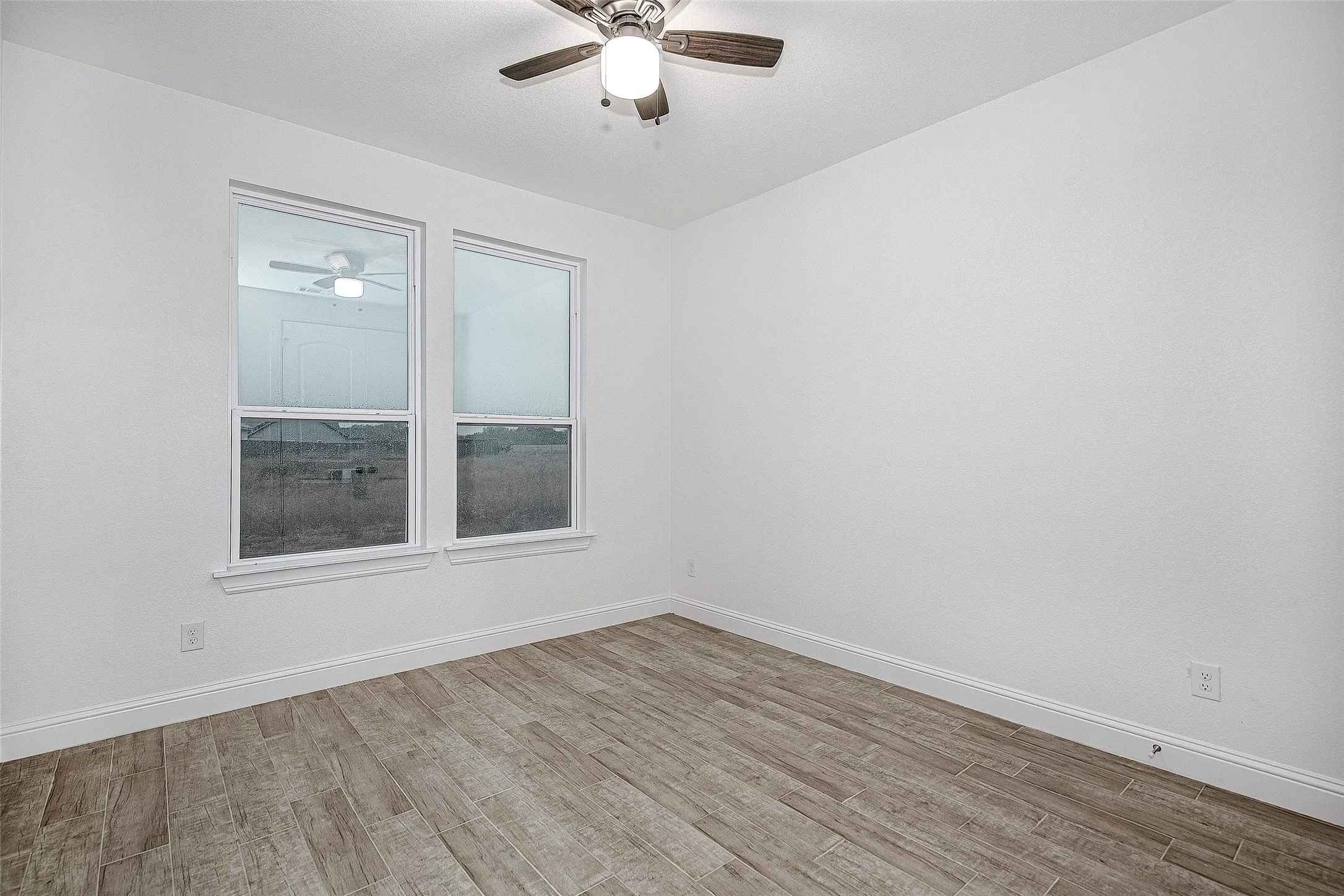 Empty room with a ceiling fan, wood finished floors, and baseboards