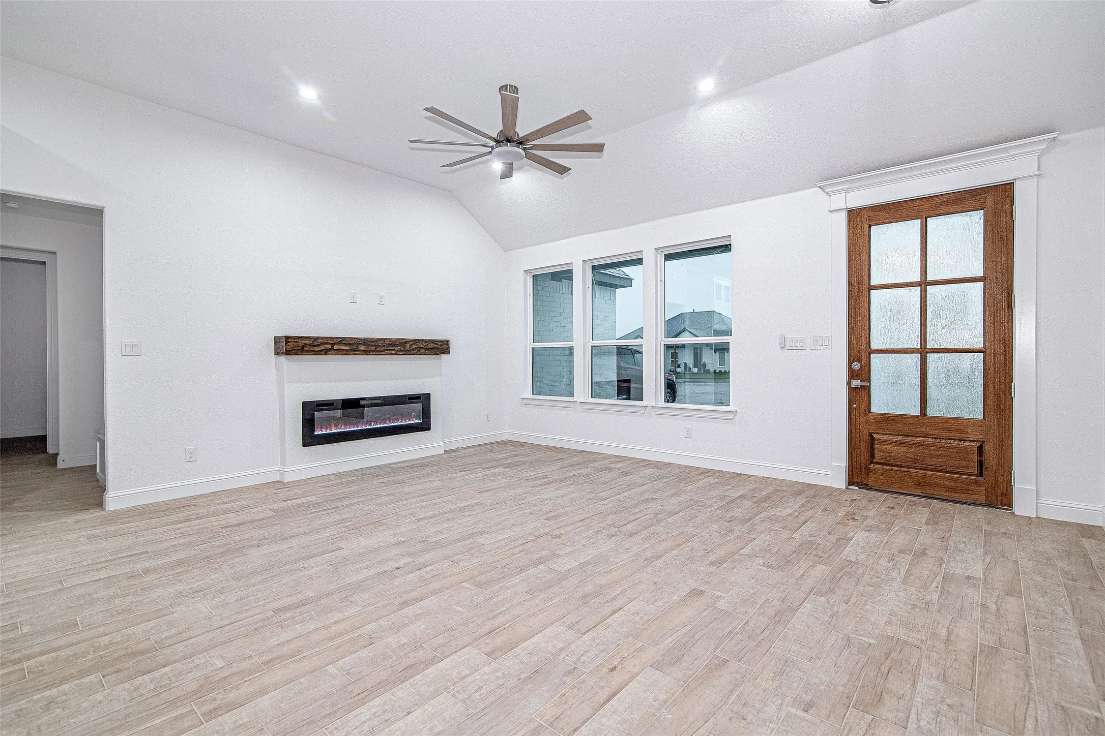 Unfurnished living room featuring a ceiling fan, vaulted ceiling, healthy amount of natural light, light wood-style floors, and a glass covered fireplace