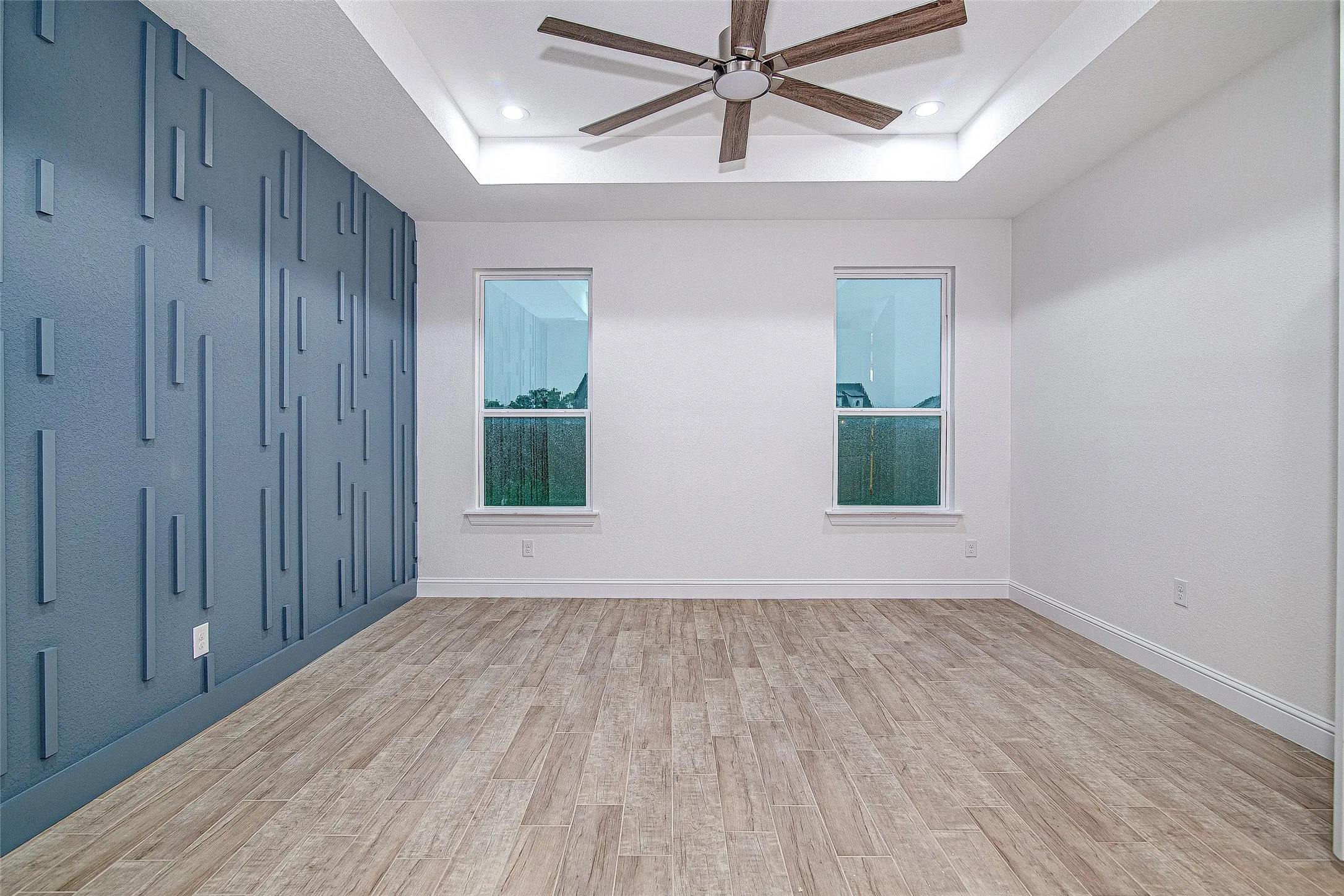 Empty room with a raised ceiling, a ceiling fan, light wood-type flooring, recessed lighting, and baseboards