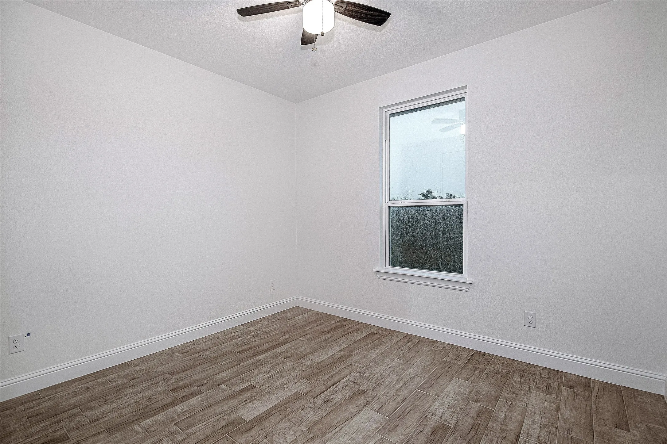 Spare room with wood finished floors, a ceiling fan, and baseboards