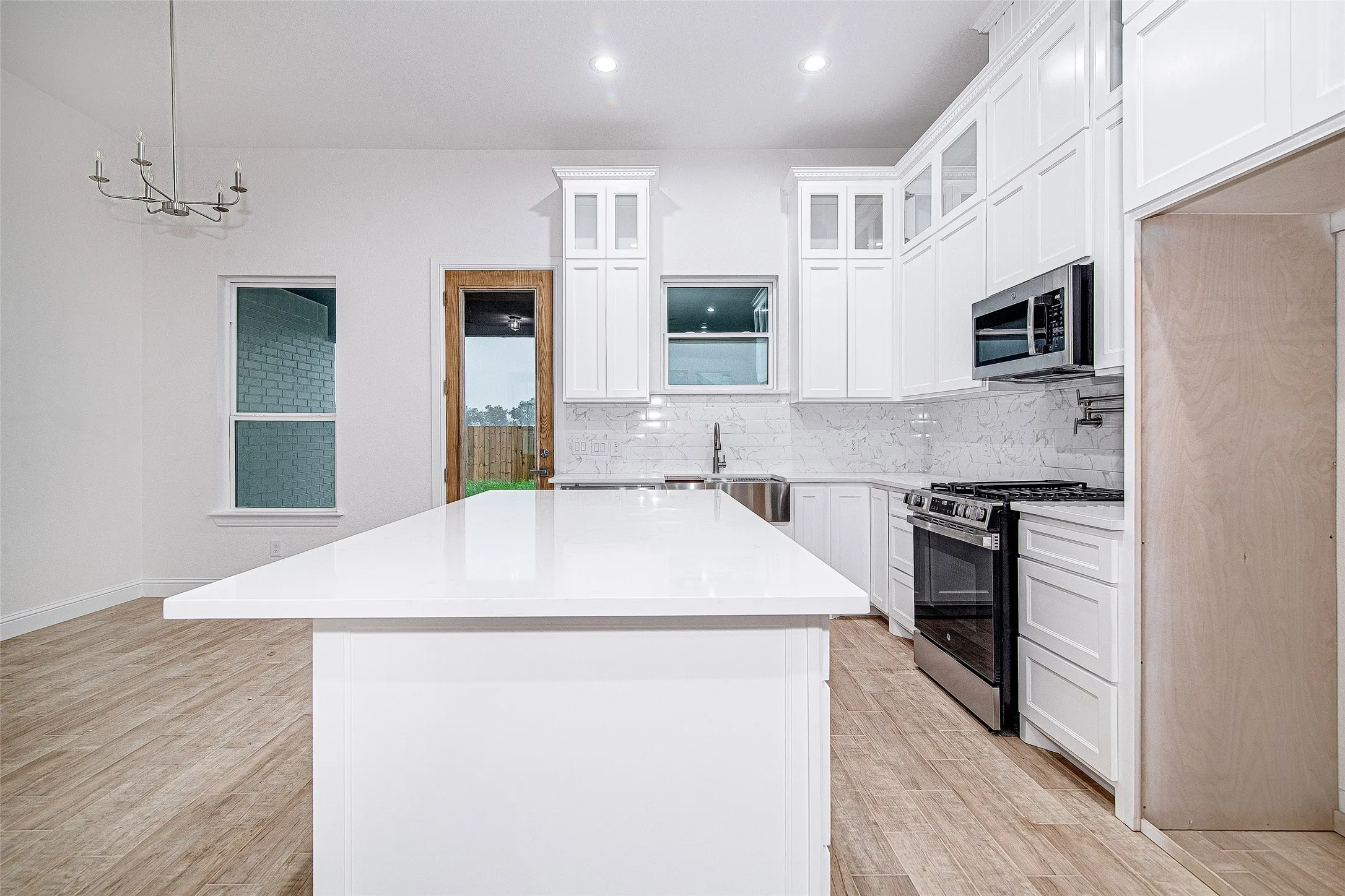 Kitchen with stainless steel appliances, light wood-type flooring, a center island, backsplash, and light countertops