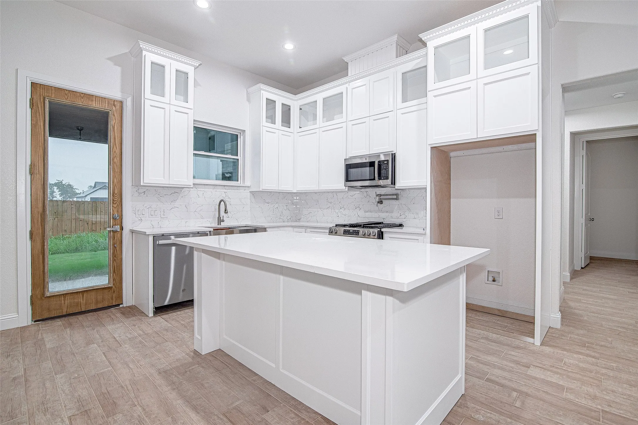 Kitchen featuring appliances with stainless steel finishes, tasteful backsplash, light wood-style flooring, white cabinets, and recessed lighting