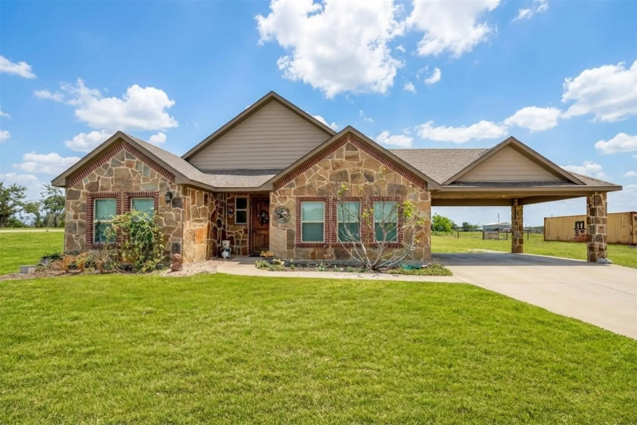 View of front of property with stone siding, a front lawn, driveway, and a carport