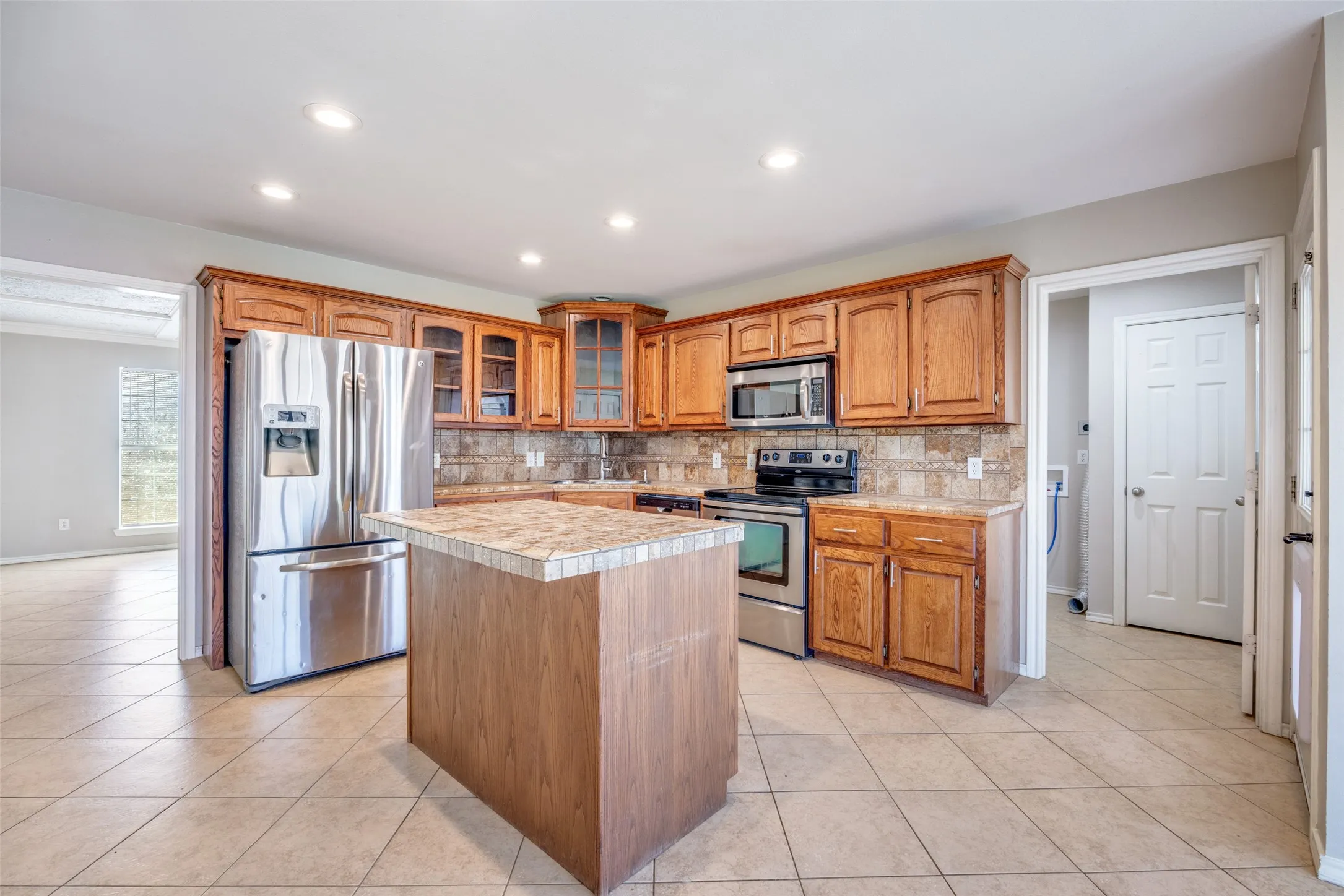 Kitchen with a center island, glass fronted cabinets, wood finish cabinetry, stainless steel appliances, and light countertops