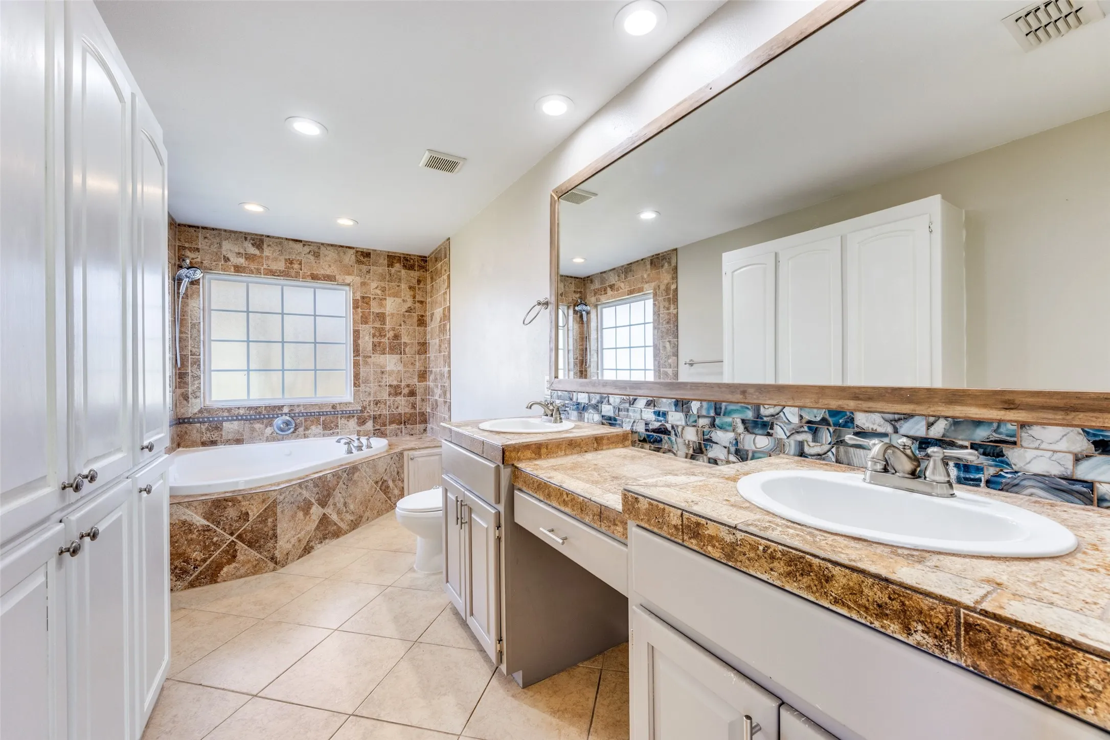 Bathroom with a bath, double vanity, light tile patterned floors, tasteful backsplash, and recessed lighting