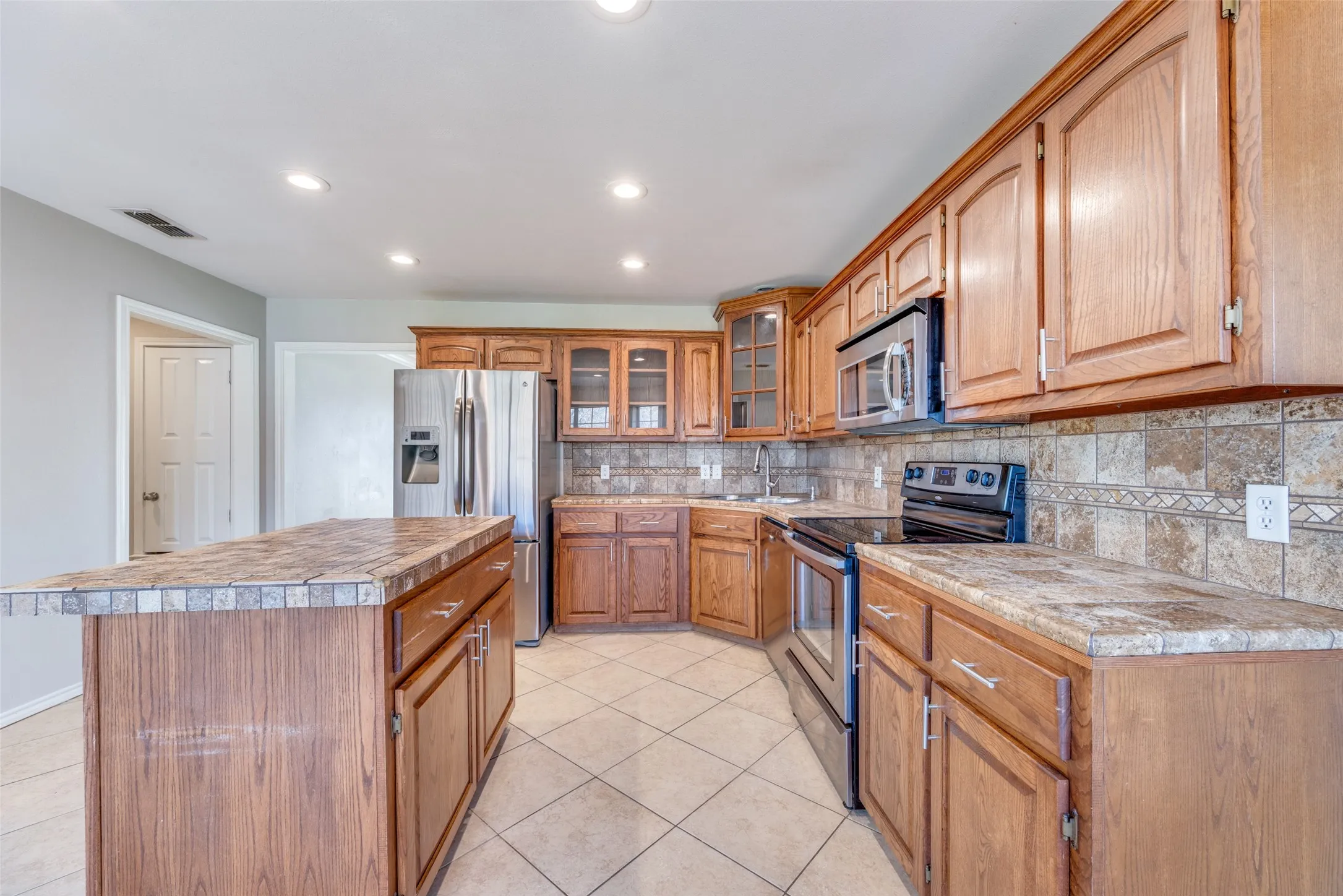 Kitchen with stainless steel appliances, glass fronted cabinets, a kitchen island, recessed lighting, and light tile patterned flooring