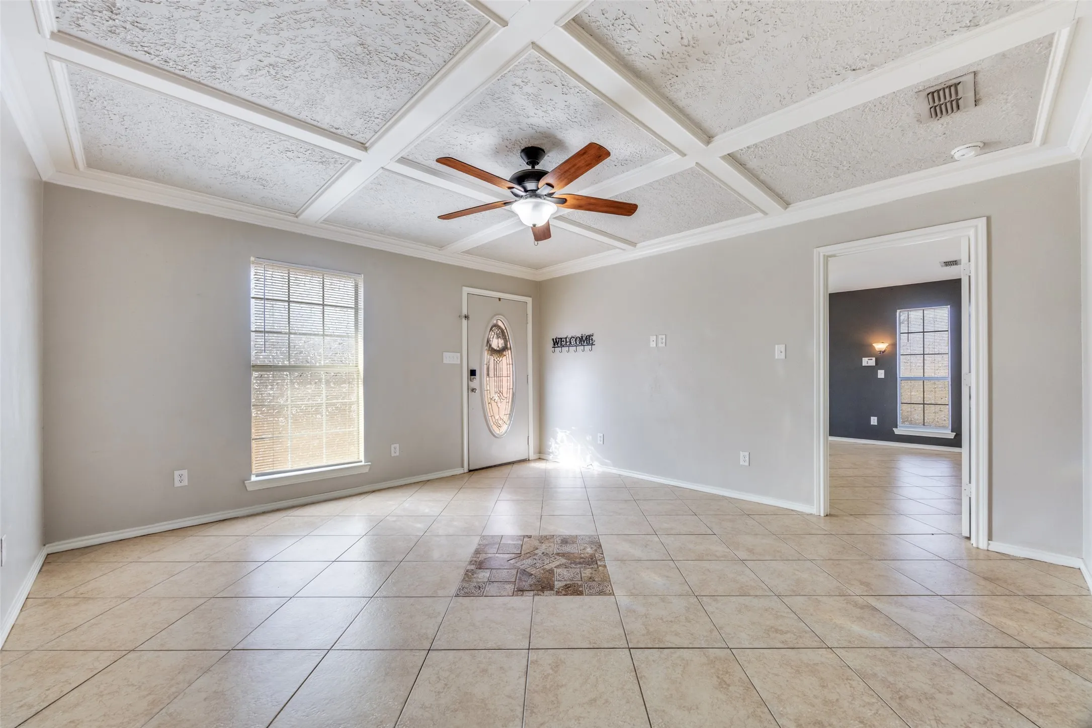 Unfurnished room with ceiling fan, coffered ceiling, ornamental molding, and light tile patterned floors