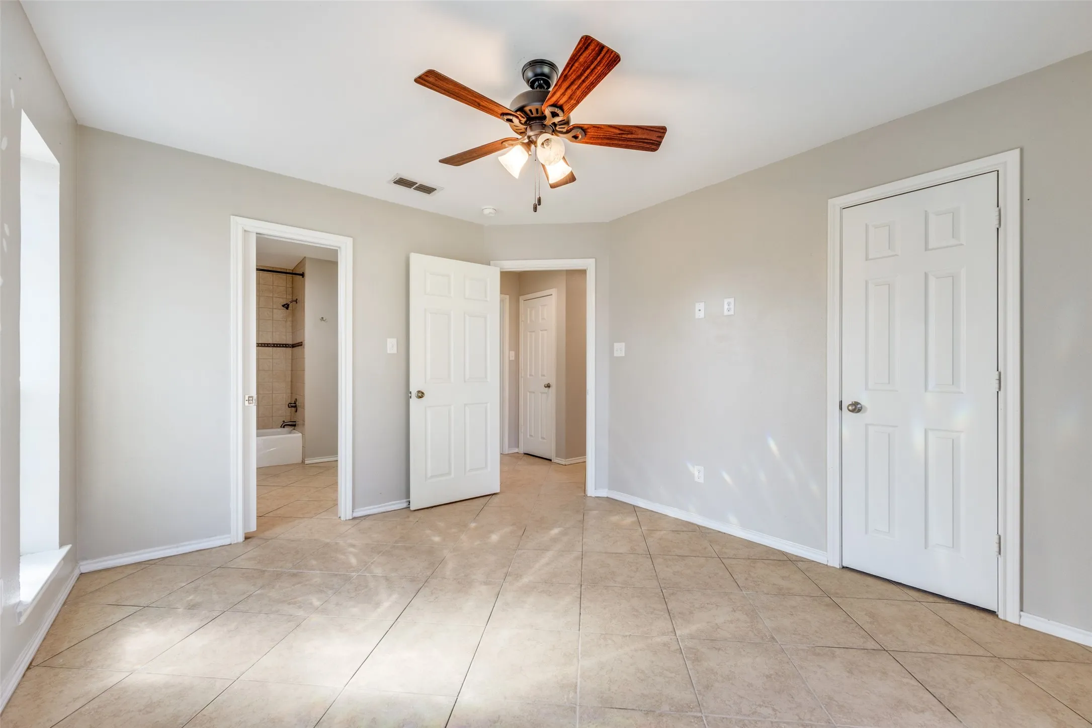 Unfurnished bedroom with a ceiling fan, ensuite bath, and light tile patterned floors