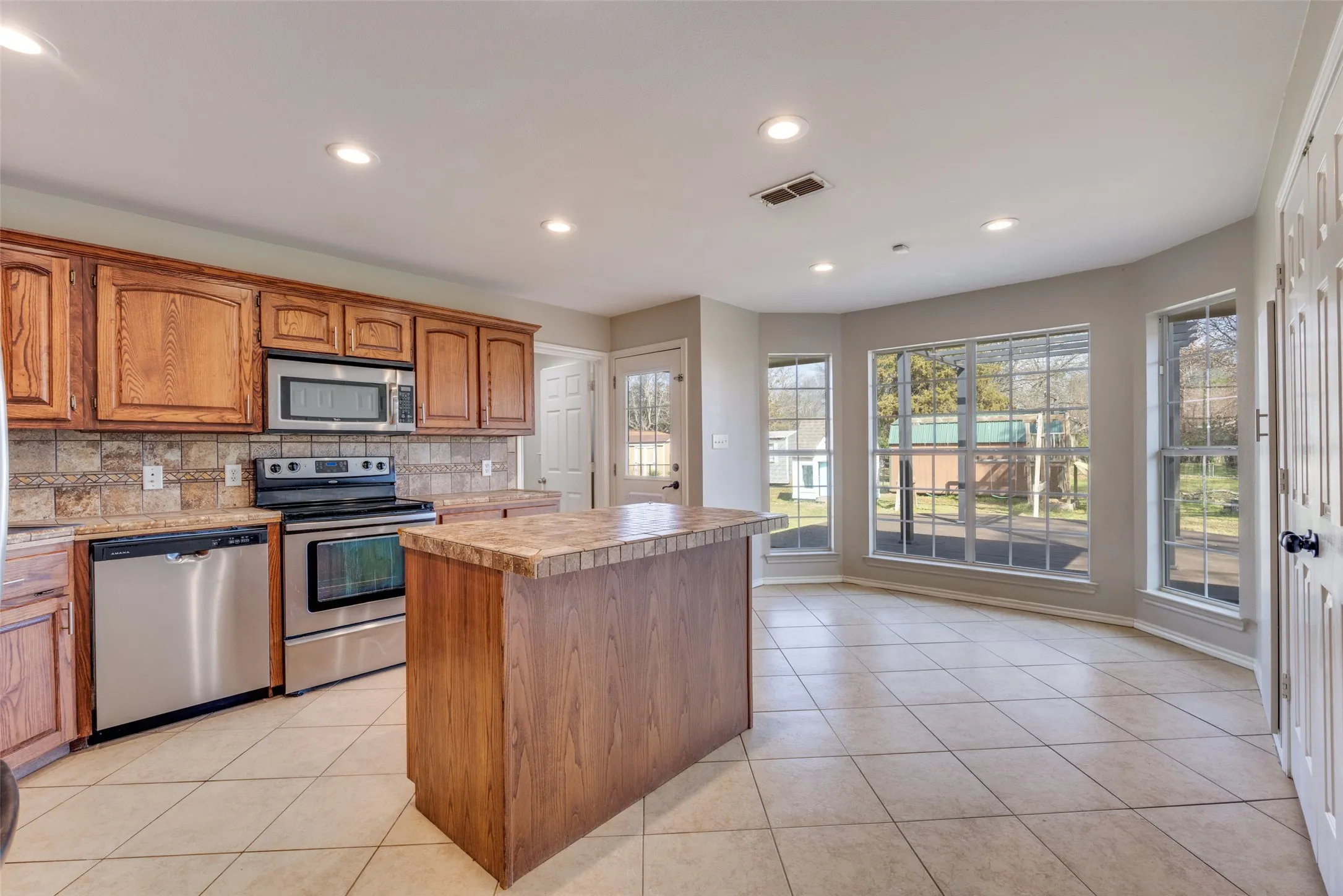 Kitchen with wood finish cabinets, stainless steel appliances, a kitchen island, light countertops, and light tile patterned floors