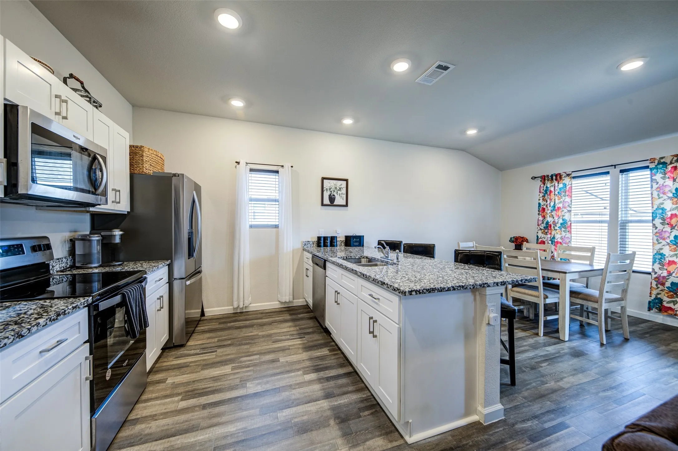 Kitchen featuring a breakfast bar area, stainless steel appliances, a peninsula, light stone counters, and white cabinets