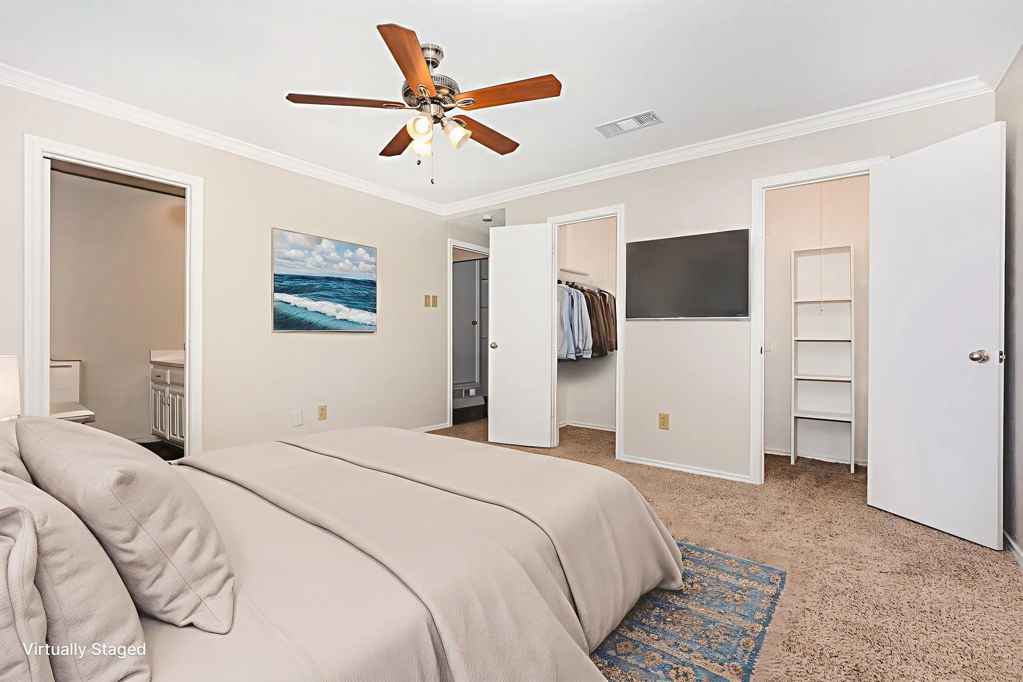 Bedroom featuring crown molding, a spacious closet, light colored carpet, ensuite bath, and a ceiling fan