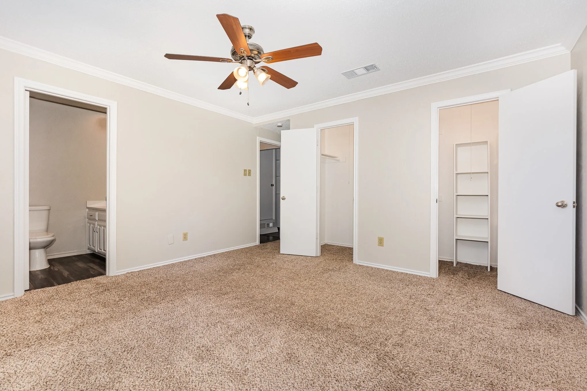 Unfurnished bedroom featuring ornamental molding, carpet flooring, ensuite bathroom, a spacious closet, and a ceiling fan