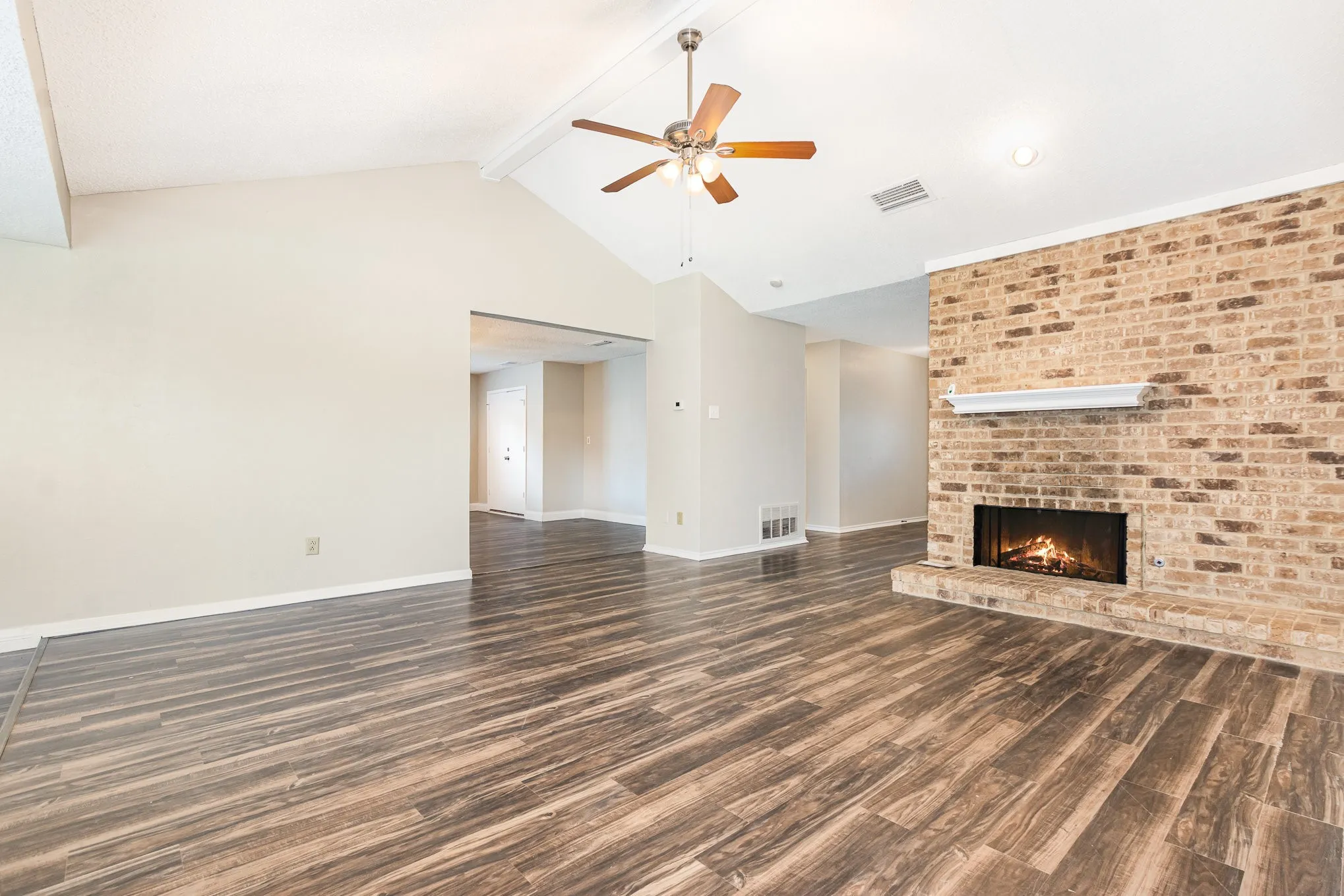 Unfurnished living room with beam ceiling, wood finished floors, ceiling fan, a fireplace, and high vaulted ceiling