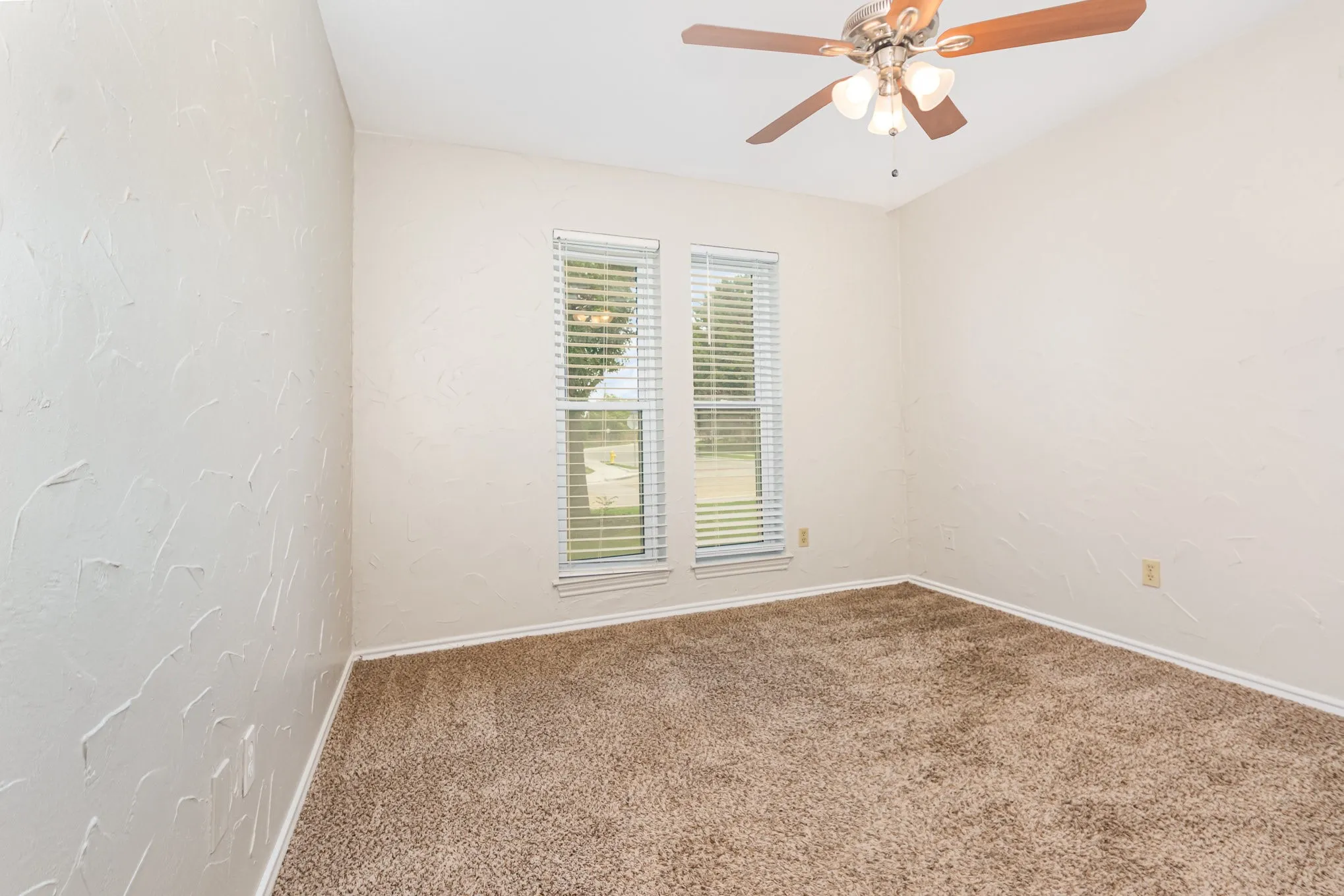 Carpeted empty room featuring ceiling fan and a textured wall