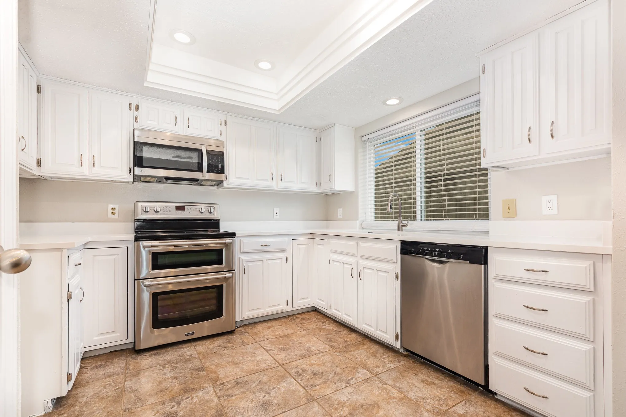 Kitchen with appliances with stainless steel finishes, recessed lighting, white cabinets, light countertops, and a raised ceiling