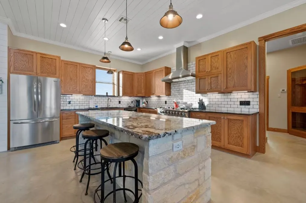 Kitchen featuring dark stone countertops, freestanding refrigerator, concrete floors, decorative light fixtures, and backsplash