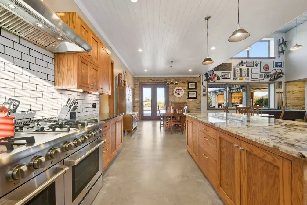 Kitchen with wall chimney range hood, double oven range, finished concrete flooring, brown cabinets, and brick wall