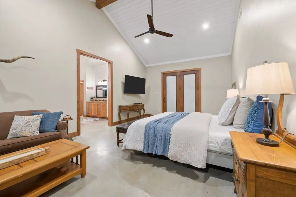 Bedroom featuring concrete flooring, a ceiling fan, beam ceiling, recessed lighting, and connected bathroom