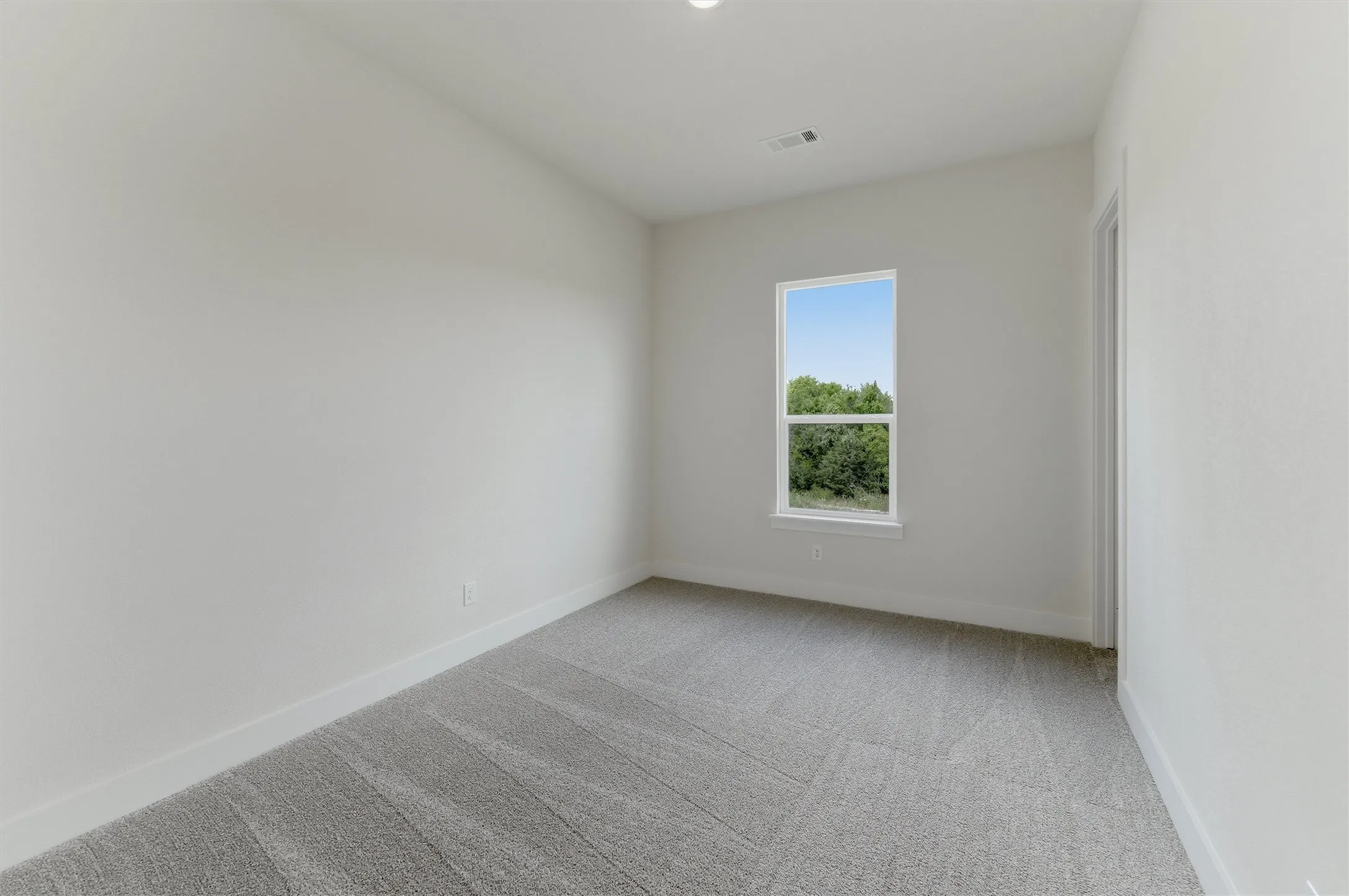 Bright interior room featuring a large window with white trim, light gray patterned carpeting, and fresh white walls